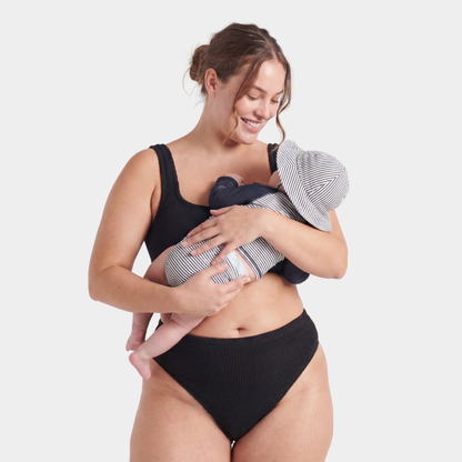 Postpartum model holding her baby, wearing the Amalfi bikini with high waisted bottoms