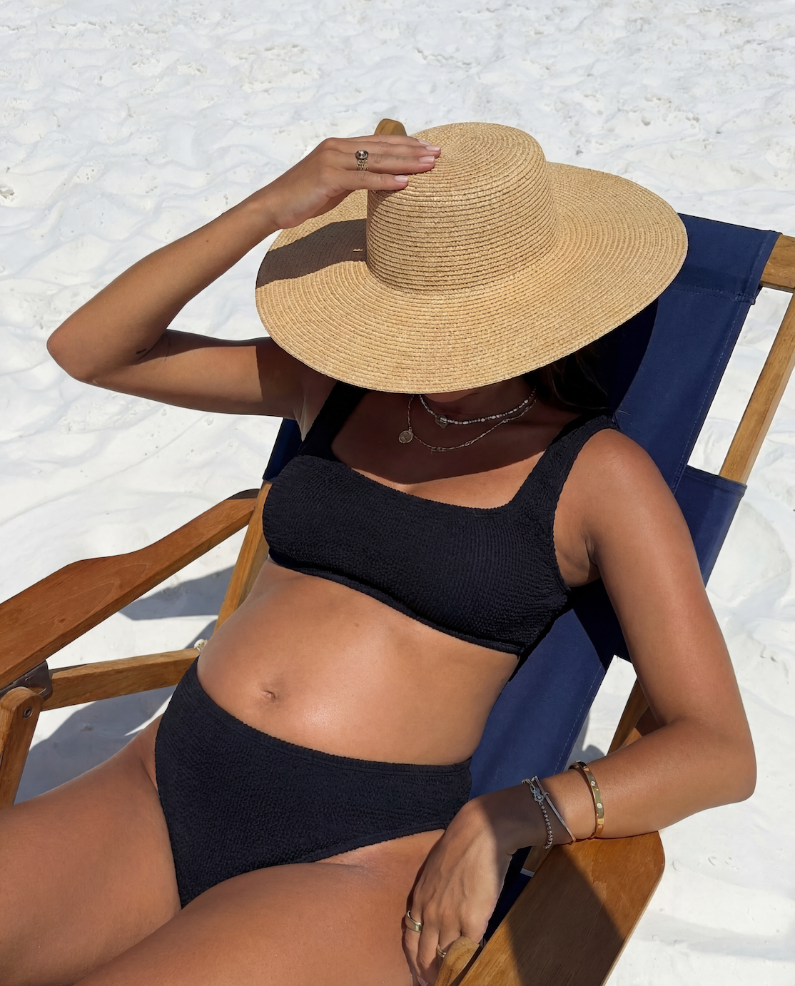 Pregnant model sitting in a deck chair wearing the high waisted crinkle bikini